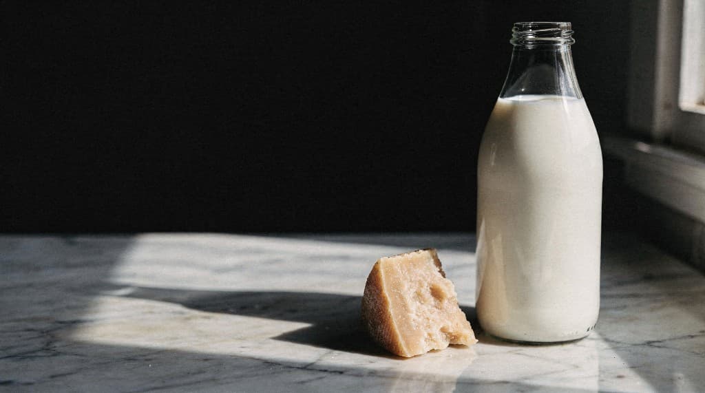 A glass bottle of milk and a wedge of aged cheese on a marble countertop